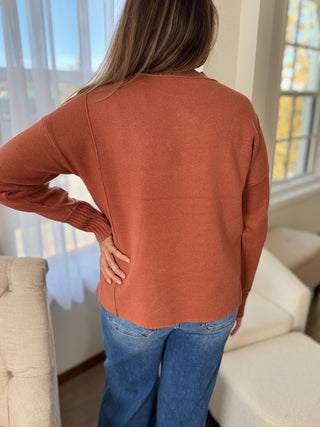 Person wearing a rust-colored sweater and blue jeans in a living room.