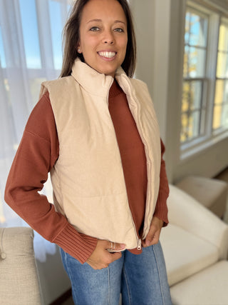 Woman wearing a beige vest over a brown sweater in a home setting