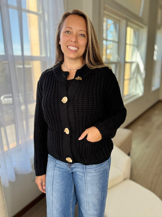 Woman wearing a black cardigan with gold buttons indoors