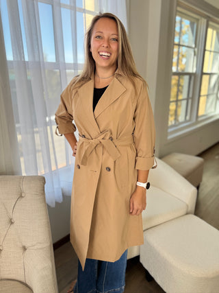 Woman wearing a beige trench coat in a living room.