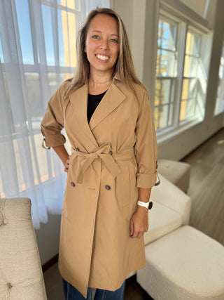 Woman wearing a beige trench coat in a modern living room.