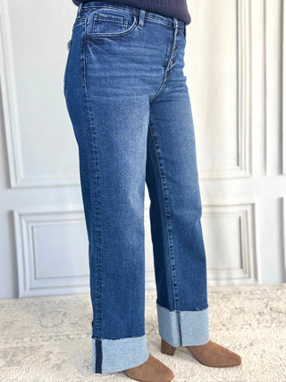 Blue jeans worn by a person on a light-colored floor with a white wall background