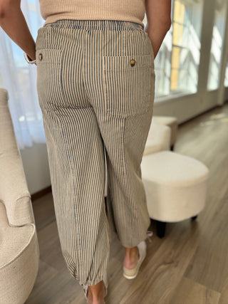 Person wearing beige striped pants in a room with furniture.
