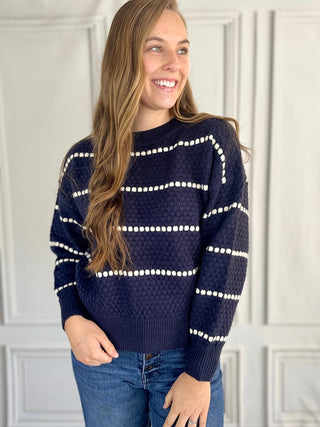 Woman wearing a navy sweater with white stripes against a white wall.