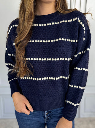Navy sweater with white pattern worn by a person against a neutral background