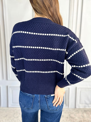 Navy sweater with white stripes worn by a person, back view, against a light-colored wall.