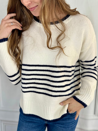 Woman wearing a white sweater with navy stripes and blue jeans.