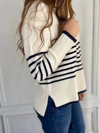 Person wearing a white sweater with navy stripes and blue jeans against a light gray background