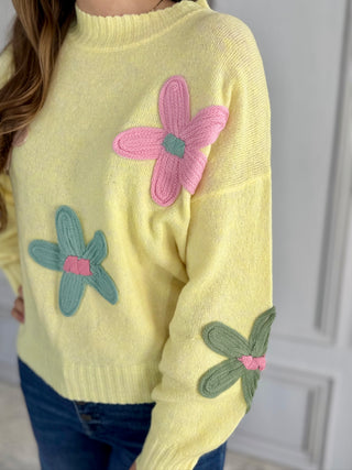 Yellow sweater with pink and green floral patterns worn by a person.
