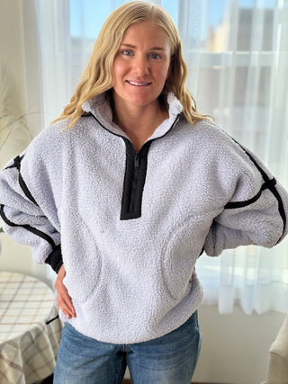 Woman wearing a gray fleece pullover with black accents in a bright room.