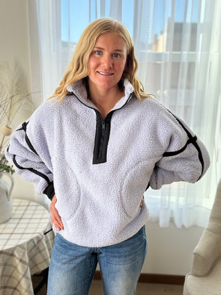 Woman wearing a gray fleece pullover with black accents indoors.