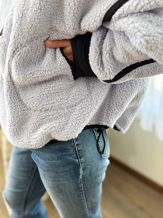 Person wearing a gray fleece jacket and blue jeans indoors.