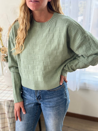 Person wearing a green sweater and blue jeans indoors