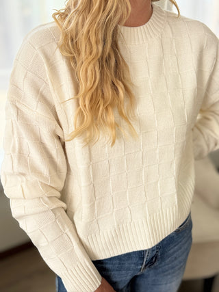 Person wearing a beige sweater and blue jeans with a blurred background