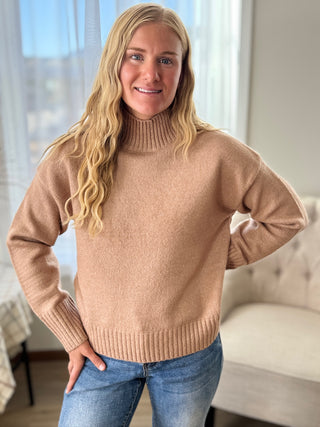 Woman wearing a beige sweater and blue jeans indoors