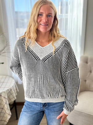 Woman wearing a black and white striped sweater and blue jeans indoors.