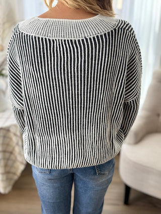 Person wearing a black and white striped sweater and blue jeans indoors.