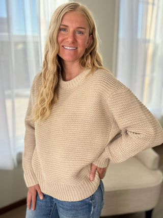 Woman wearing a beige sweater and blue jeans indoors with light background