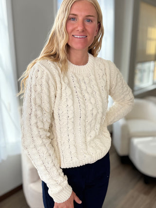 Woman wearing a cream cable knit sweater in an indoor setting