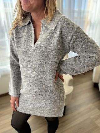 Person wearing a gray sweater in a room with light-colored curtains.