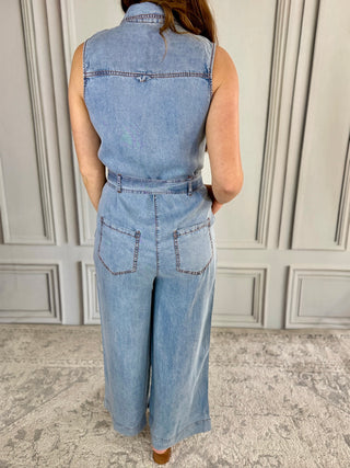 Person wearing a denim jumpsuit standing against a neutral wall.