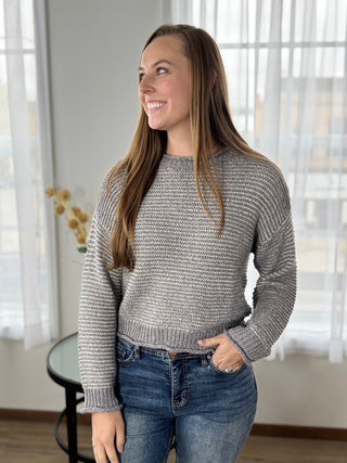 Woman wearing a gray sweater and blue jeans indoors