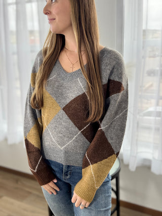 Woman wearing a gray, brown, and yellow diamond pattern sweater indoors.