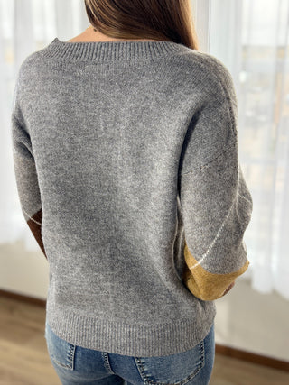 Person wearing a gray sweater with yellow cuffs and hem in a bright room.