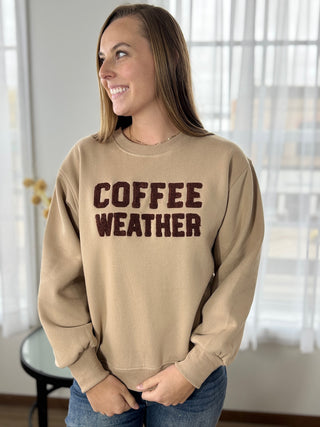 Woman wearing a beige sweatshirt with 'COFFEE WEATHER' text in a home setting