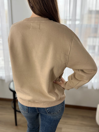 Person wearing a beige sweater and blue jeans standing indoors with a blurred background