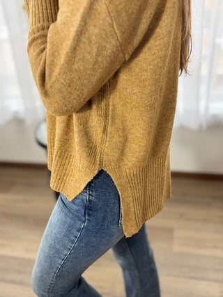 Person wearing a mustard yellow sweater and blue jeans indoors.