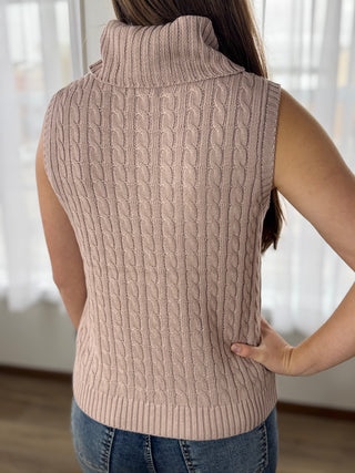 Person wearing a beige knitted vest with a blurred background