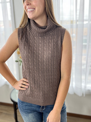 Woman wearing a brown cable knit sleeveless sweater in a bright room.