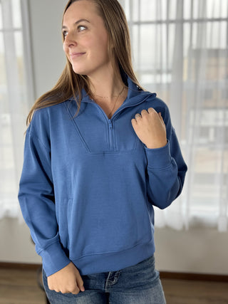 Woman wearing a blue pullover with a quarter zip in a bright room.