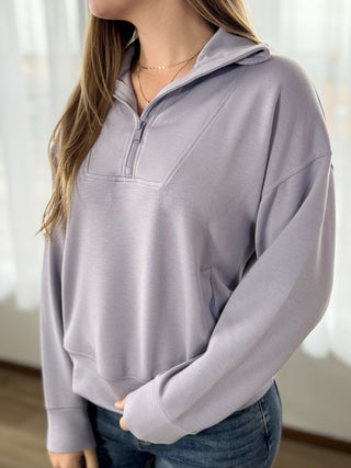 Person wearing a light gray pullover with a quarter zip in a neutral setting