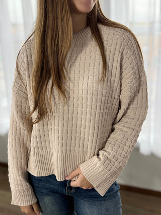 Person wearing a beige ribbed sweater and blue jeans indoors.