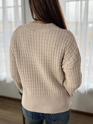 Person wearing a beige sweater with a blurred background