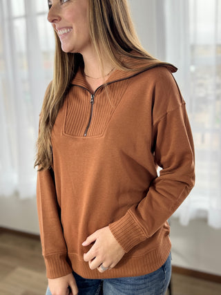 Woman wearing a brown sweater with a zipper in a bright room.