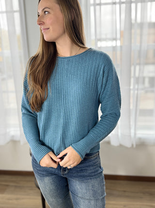 Woman wearing a blue sweater and jeans indoors with a neutral background