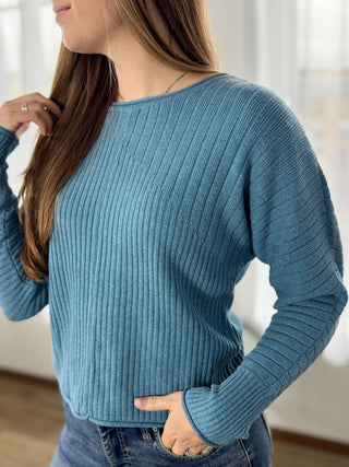 Woman wearing a blue ribbed sweater with a blurred background