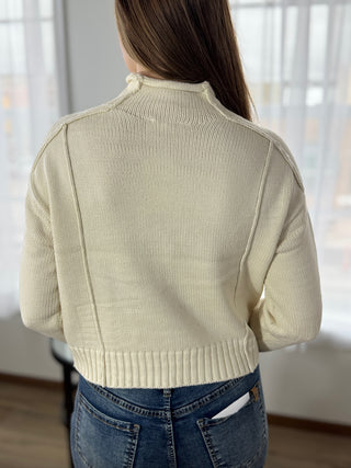 Person wearing a beige sweater and blue jeans indoors