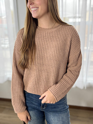 Woman wearing a brown knitted sweater and blue jeans indoors.