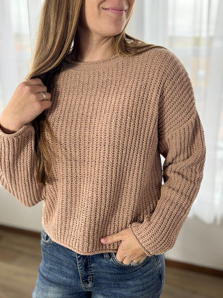 Person wearing a beige knitted sweater and blue jeans indoors.