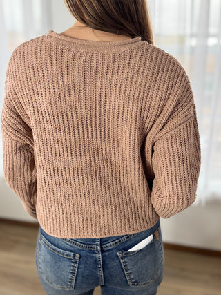 Person wearing a beige knitted sweater and blue jeans indoors.