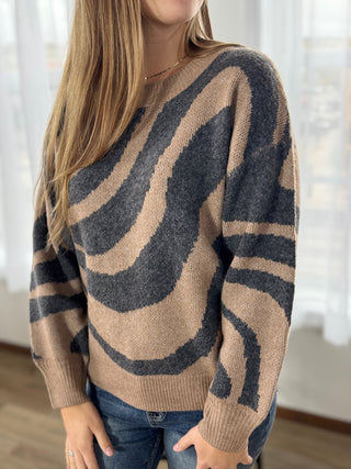 Person wearing a brown sweater with abstract black design indoors