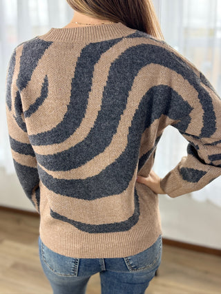 Person wearing a beige sweater with black wavy pattern indoors