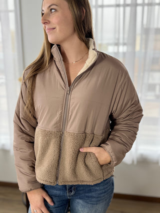 Woman wearing a brown puffer jacket with a blurred indoor background