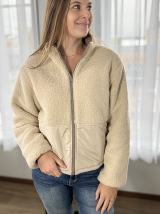 Woman wearing a beige fleece jacket indoors with a neutral background