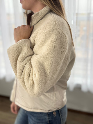 Person wearing a beige fleece jacket indoors with a blurred background