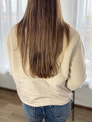 Person wearing a beige fleece jacket and blue jeans with long brown hair, standing indoors.